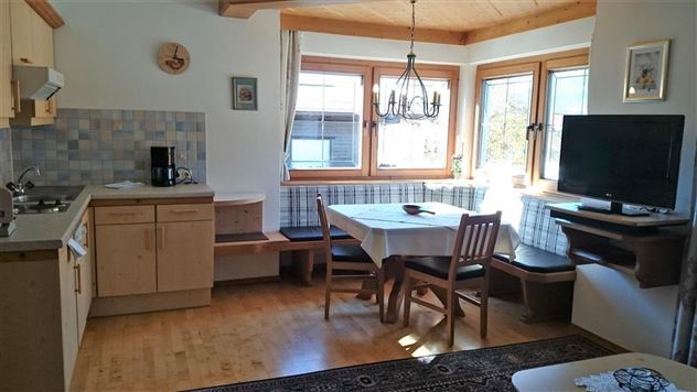A bright kitchen with wooden shelves and a dining table. Large windows provide plenty of natural light.
