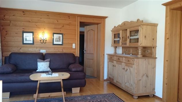 A cozy living room with a brown sofa and a wooden table.  
On the wall, there are wooden panelings and picture frames, as well as a wooden sideboard.