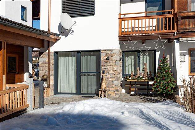 Een modern huis met een met sneeuw bedekte tuin. Voor het huis staat een kerstboom en feestelijke decoratie.