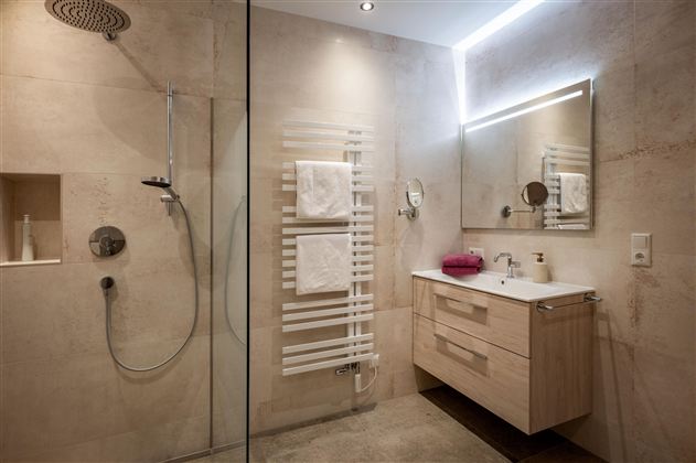 Een moderne badkamer met een grote douche en een elegante houten kast. De muren zijn in lichte tinten gehouden en er zijn verse handdoeken.