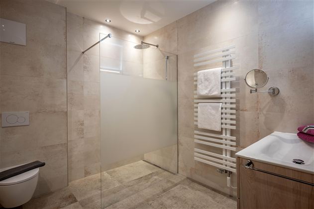 Een moderne badkamer met een inloopdouche en elegante tegels. Handdoeken hangen aan een handdoekhouder en een wastafel met een houten onderkast is zichtbaar.