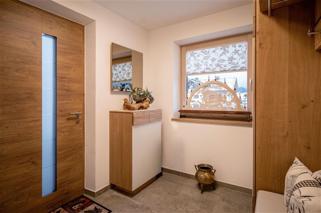 Een moderne entrée met houten details en een groot raam. De inrichting is eenvoudig en uitnodigend vormgegeven.