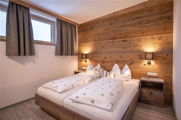 Een sfeervolle slaapkamer met twee bedden en een modern houten wandontwerp. De ruimtes zijn helder en vriendelijk met ramen en subtiele verlichtingsaccenten.