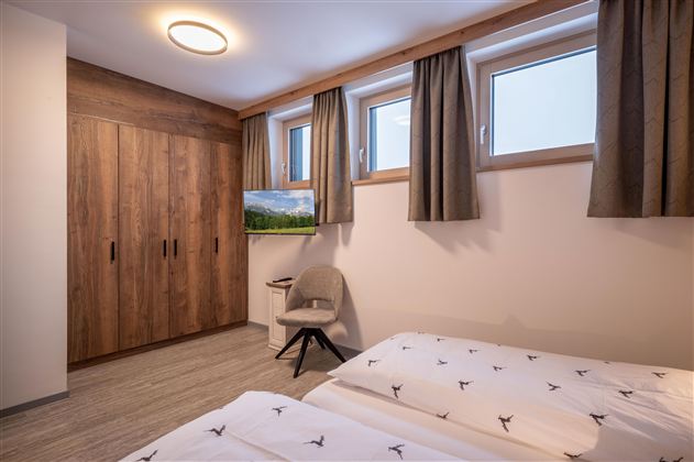 Een moderne slaapkamer met twee eenpersoonsbedden en een grote houten kast. De ramen zijn voorzien van gordijnen en een televisie completeert de inrichting.