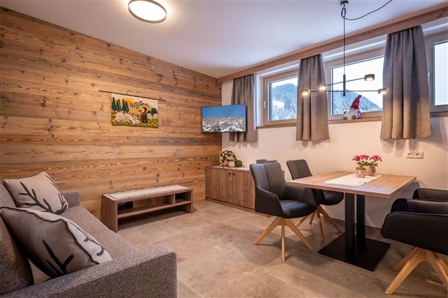 Een moderne woon- en eetkamer met houten wanden. Er is een eetgedeelte met een tafel en stoelen, evenals een gezellige bank.