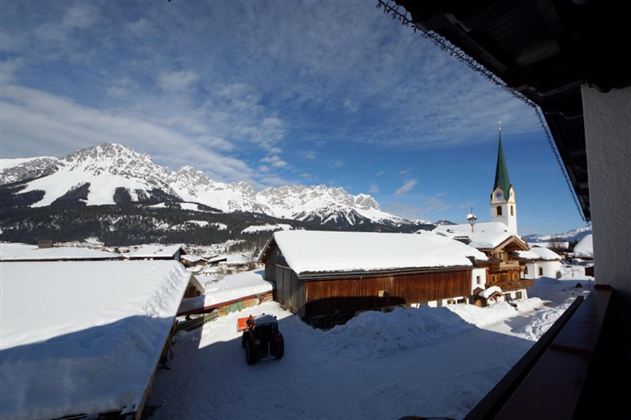 Ein malerisches Dorf im Schnee mit beeindruckenden Bergen im Hintergrund. Die Kirche mit dem grünen Turm fügt eine charmante Note hinzu.