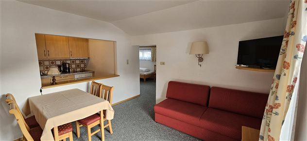 A cozy living room with a red sofa and a dining table. The open kitchen is well-equipped and has wooden cabinets.