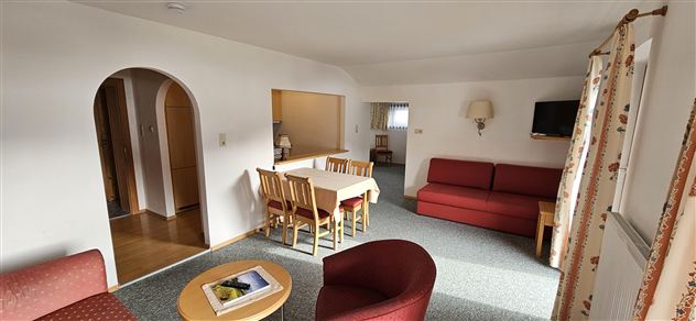 A bright living room with a red sofa and a dining table. The atmosphere is cozy and inviting.