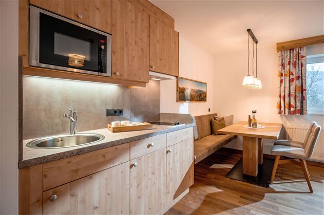 Moderní kuchyňská linka z dřeva s mikrovlnnou troubou a dřezem. V pozadí se nachází útulný jídelní kout se stolem a sedačkou.