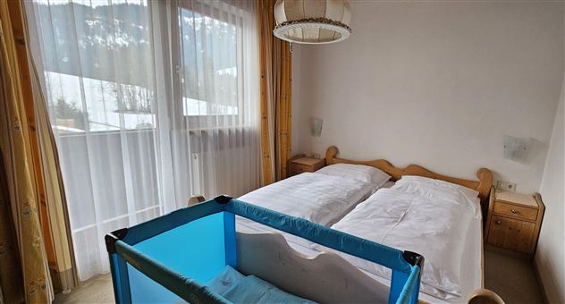 A bright bedroom with two beds and a crib. Large windows let in a lot of light.