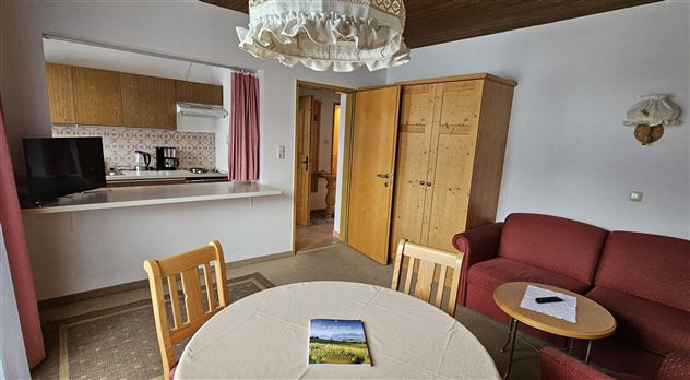 A cozy apartment with an open kitchen and a dining area. The room features a red sofa and a table with chairs.