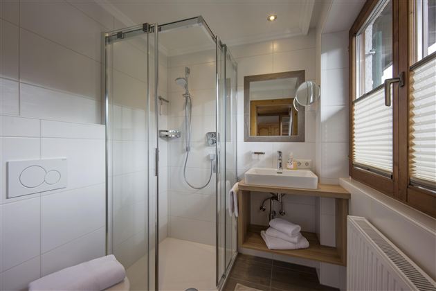 A modern bathroom with a glass shower and a wooden sink. The windows let in plenty of daylight.