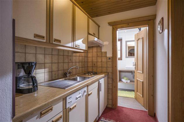 A small kitchen with light wooden cabinets and modern amenities. The space is tidy and inviting with access to another room.