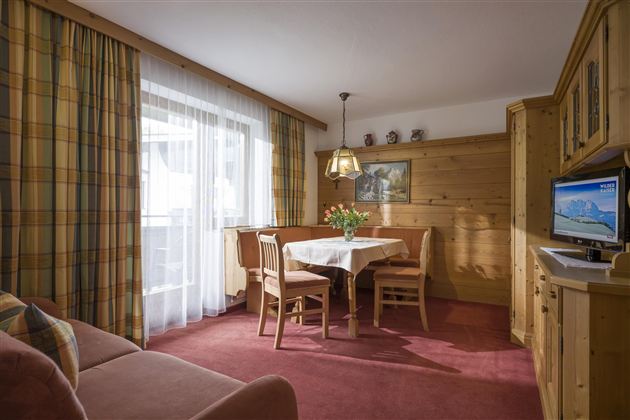 A cozy living space with wooden furniture and a dining table. Large windows let in plenty of light and offer an inviting view.