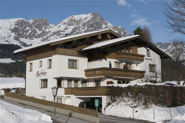 Ein gemütliches Gebäude im Alpenstil, umgeben von schneebedeckten Bergen. Der Himmel ist klar, und es liegt Schnee auf dem Boden.