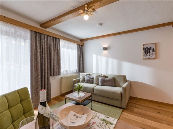 Ein heller Wohnraum mit einem gemütlichen Sofa und einem kleinen Tisch. Große Fenster lassen viel Tageslicht herein.