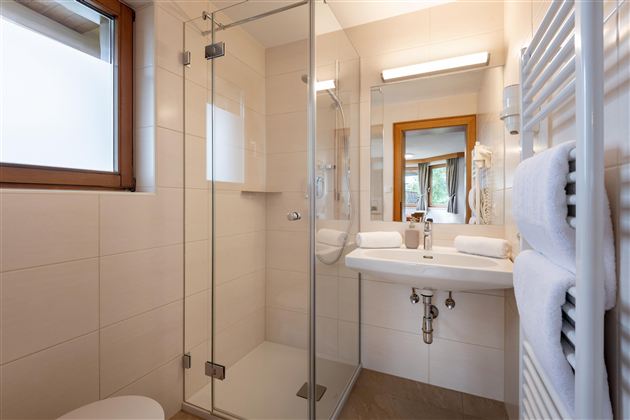 Ein modernes Badezimmer mit einer Glasdusche und einem Waschbecken. Helle Fliesen und ein großer Spiegel sorgen für eine freundliche Atmosphäre.