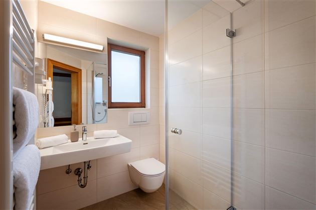 Ein modernes Badezimmer mit Dusche, Waschbecken und Spiegel. Helle Fliesen und natürliche Beleuchtung durch ein Fenster sorgen für eine freundliche Atmosphäre.