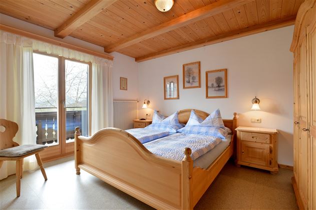 Ein gemütliches Schlafzimmer mit Holzdecken und einem Doppelbett. Große Fenster lassen viel Tageslicht hinein und bieten einen Blick nach draußen.