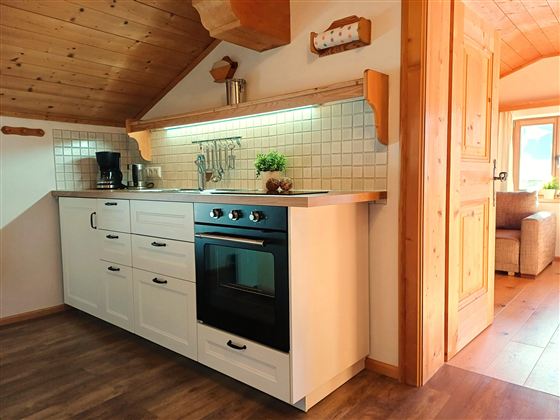 A modern kitchen with white cabinets and a stove. The room has a cozy atmosphere and plenty of daylight.