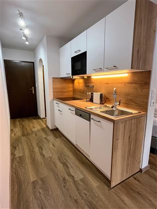 Eine moderne Küche mit weißen Schränken und Holzverkleidung. Der Boden ist aus Holz und es gibt eine angenehme Beleuchtung.