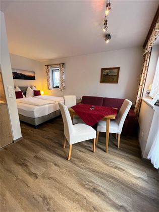 Ein gemütliches Zimmer mit zwei Betten und einem Tisch. Der Raum ist hell und einladend, mit Holzfußboden und dekorativen Fenstern.