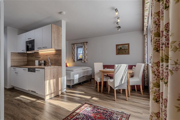 Eine moderne, helle Wohnung mit offener Küche und Essbereich. Der Raum ist gemütlich eingerichtet und hat große Fenster, die für viel Licht sorgen.