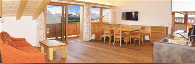 Ein modernes Wohnzimmer mit Holzmöbeln und einem Essbereich. Große Fenster bieten einen Blick auf die Berge.