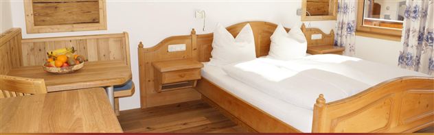 Ein gemütliches Zimmer mit einem Doppelbett und hellen Holzmöbeln. Ein Tisch mit einer Obstschale ergänzt die freundliche Atmosphäre.