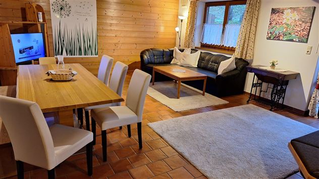 A cozy living room with a dining table and chairs. In the background, a sofa and decorations can be seen.