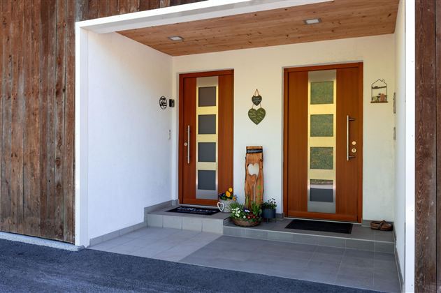 Der Eingang zu einem modernen Haus mit zwei Holztüren. Neben den Türen steht eine dekorierte Pflanze auf der Veranda.