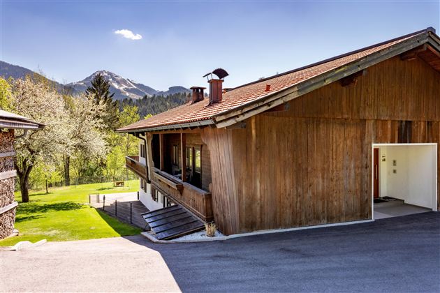 Ein modernes Holzhaus in den Bergen mit einer schönen Aussicht auf die umliegende Landschaft. Der Himmel ist blau und es ist ein sonniger Tag.