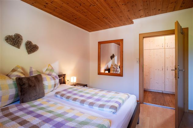 Ein gemütliches Schlafzimmer mit zwei Betten und bunten Decken. Im Hintergrund sind ein Spiegel und ein Kleiderschrank zu sehen.