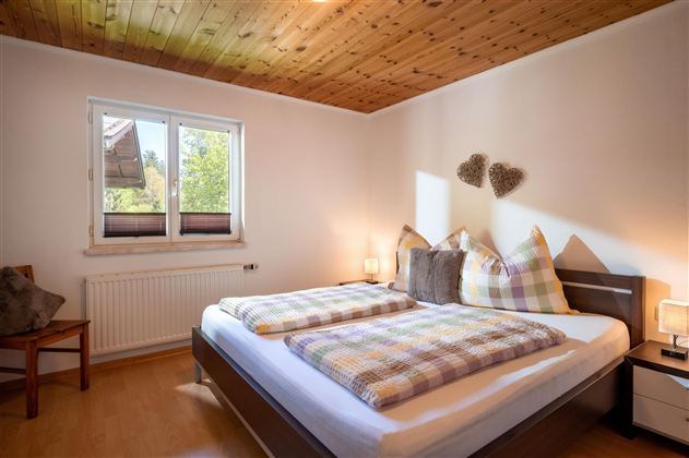 Ein helles Schlafzimmer mit einem Doppelbett und karierten Kissen. Neben dem Bett steht ein Stuhl und ein Fenster lässt natürliches Licht herein.