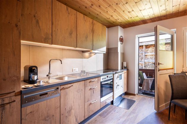Eine moderne Küche mit Holzschränken und hellen Wänden. Die Tür öffnet sich zu einem kleinen Außenbereich.