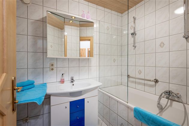 A modern bathroom with white tiles and a bathtub. Turquoise towels are placed on the sink.