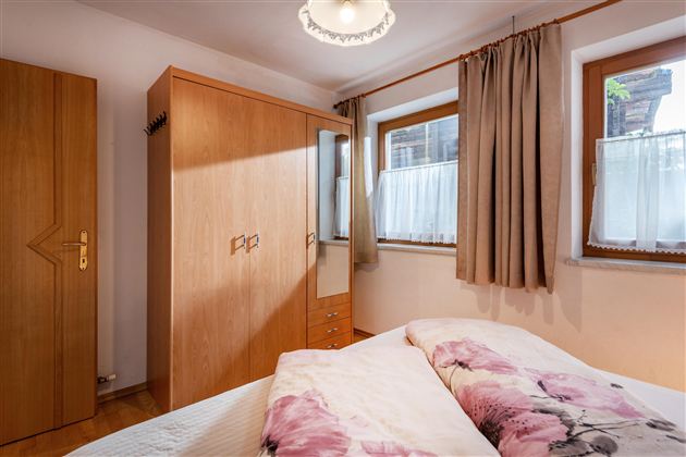 A cozy bedroom with a large bed and wooden furniture. The room has windows with curtains and a pleasant lighting.