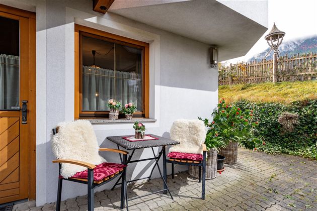 A cozy outdoor area with a small table and two chairs. Surrounded by plants and a bright, inviting atmosphere.