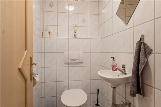 A small, clean bathroom with white tiles. It includes a toilet, a sink, and a towel rack.