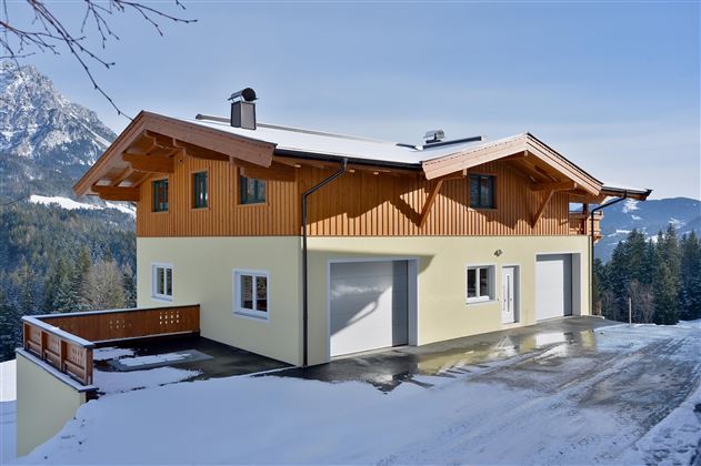 A modern house in a snow-covered landscape. In the background, there are mountains and a clear sky.