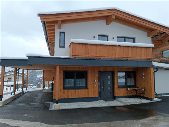 Ein modernes Holzhaus mit einem großen Balkon. Es ist von Schnee umgeben und hat eine einladende Fassade.