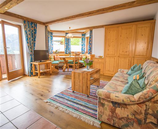 A cozy living room with wooden floors and rustic furniture. Large windows provide plenty of daylight and a view of nature.