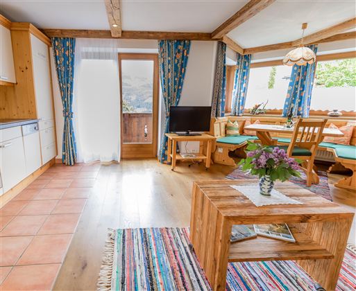 A cozy living space with wooden details and colorful curtains. The room is bright and inviting, with a small table and a television.