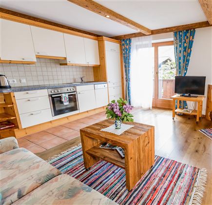 A cozy apartment with a modern kitchen and a living room. The space is bright and friendly, with a wooden coffee table and colorful curtains.