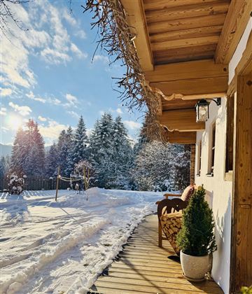A cozy terrace of a house in the snow with a view of snow-covered trees. The sky is clear and the sun is shining.