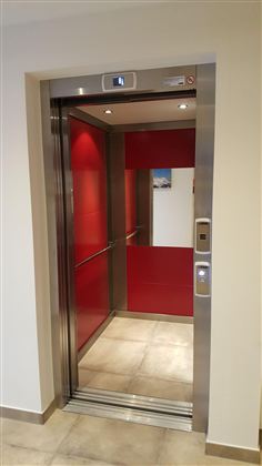 Ein moderner Aufzug mit roten Wänden und glänzenden Metallverkleidungen. Der Aufzug ist offen und bereit für Passagiere.