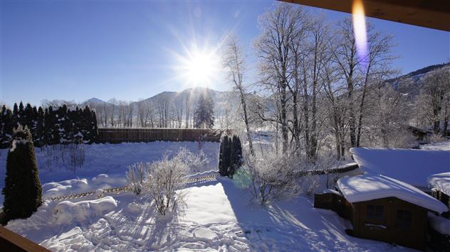Eine wunderschöne Winterlandschaft mit schneebedeckten Bäumen und einem strahlenden Sonnenschein. Im Hintergrund sind sanfte Hügel sichtbar.