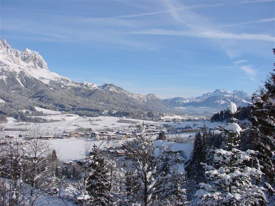 Eine verschneite Landschaft mit Bergen und einem kleinen Dorf in der Talsohle. Der klare Himmel verleiht der winterlichen Szenerie eine ruhige Atmosphäre.