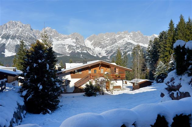 Ein idyllisches Chalet in einer schneebedeckten Landschaft. Im Hintergrund sind beeindruckende Berggipfel zu sehen.