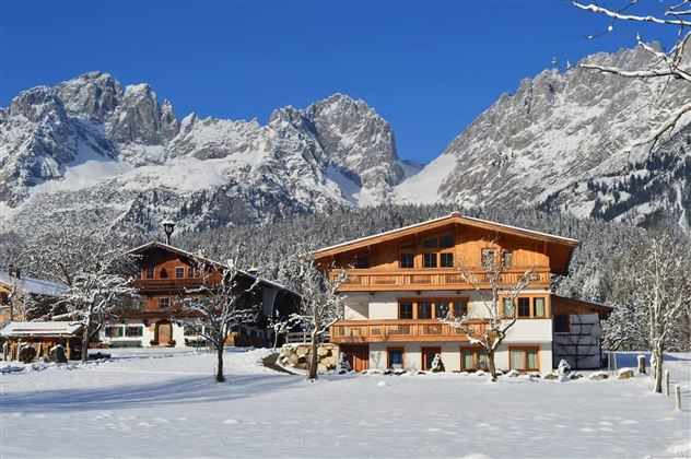 A picturesque winter village with snow-covered mountains in the background. The traditional wooden houses are surrounded by an idyllic snowy landscape.